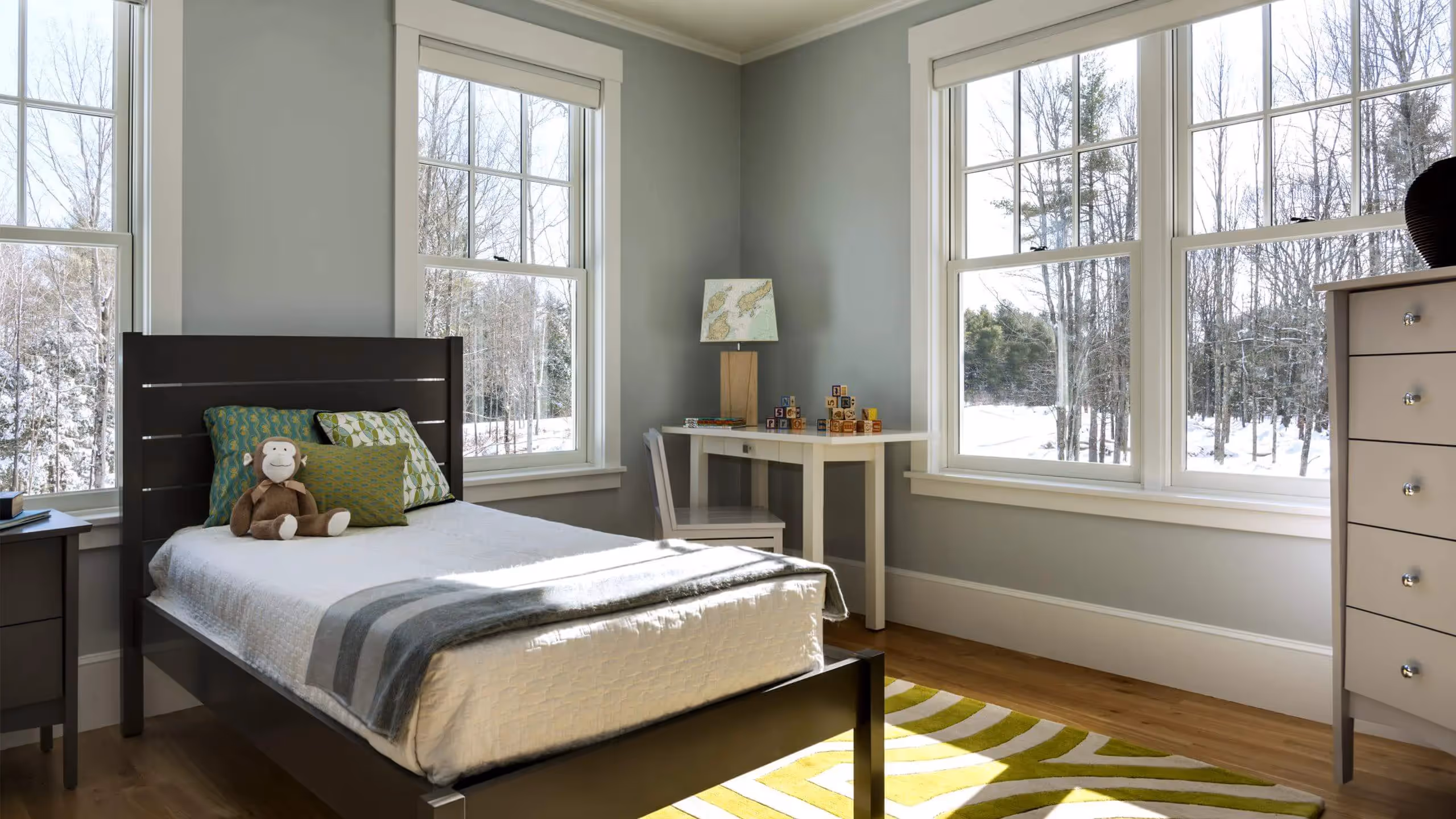 Cozy bedroom with large windows overlooking snowy winter forest landscape