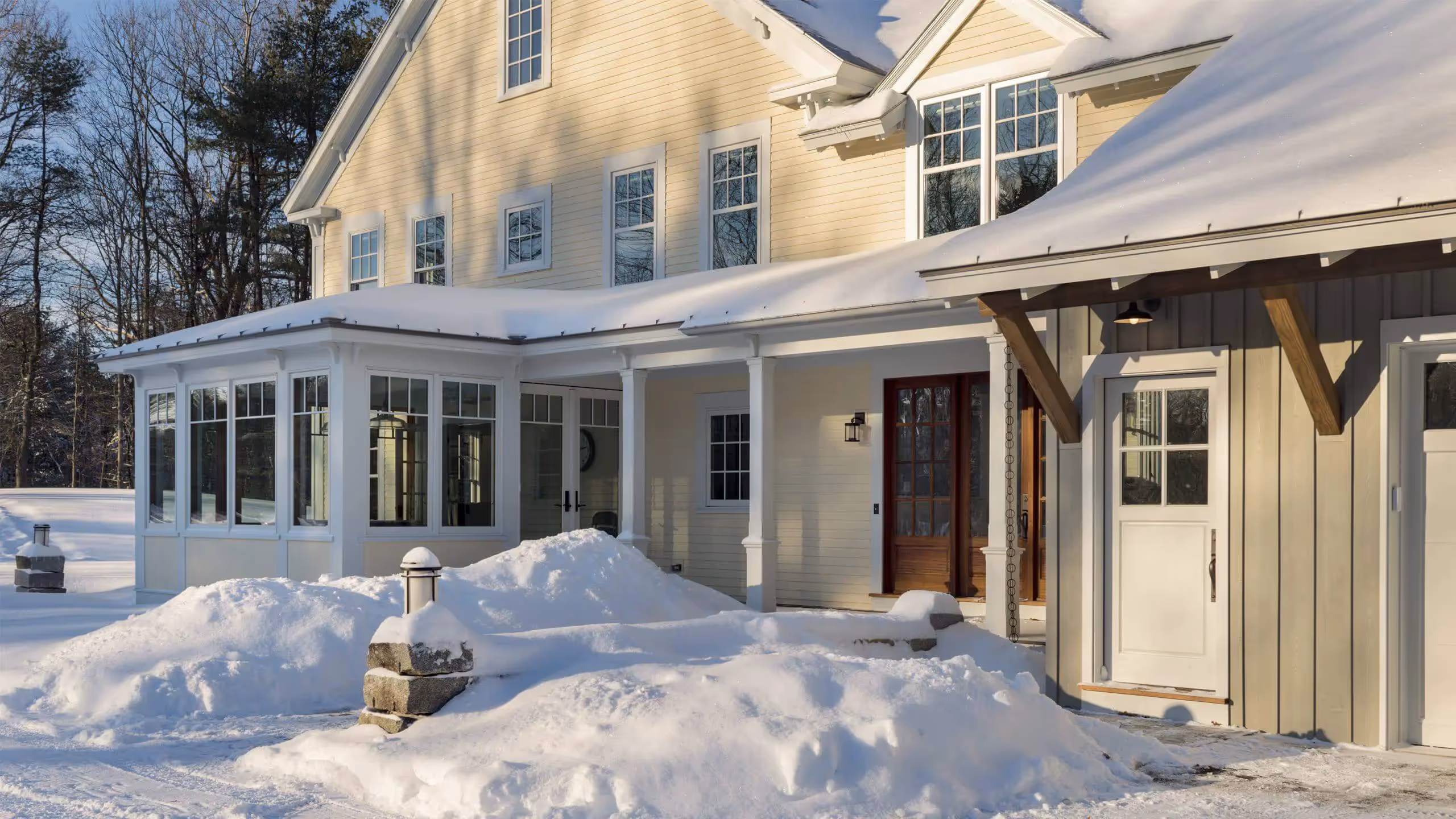 Snowy winter day at a yellow farmhouse with a wraparound porch