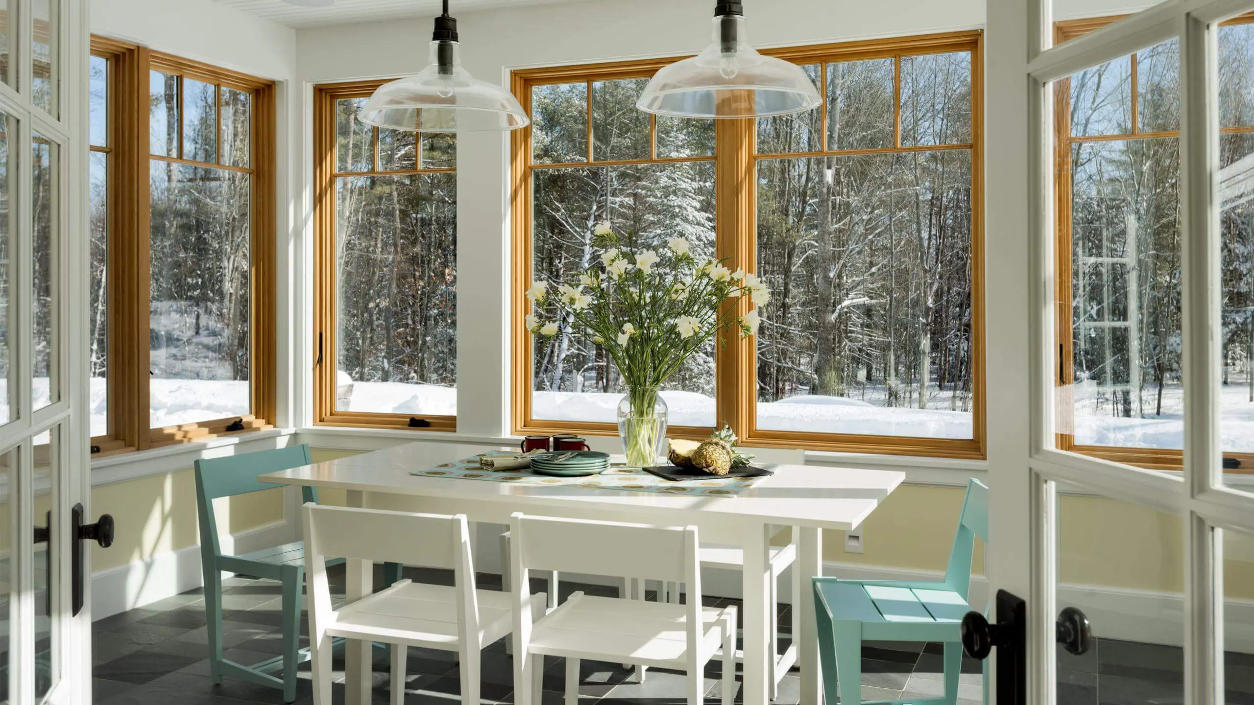 Bright sunroom with white table, blue chairs overlooking snowy winter forest