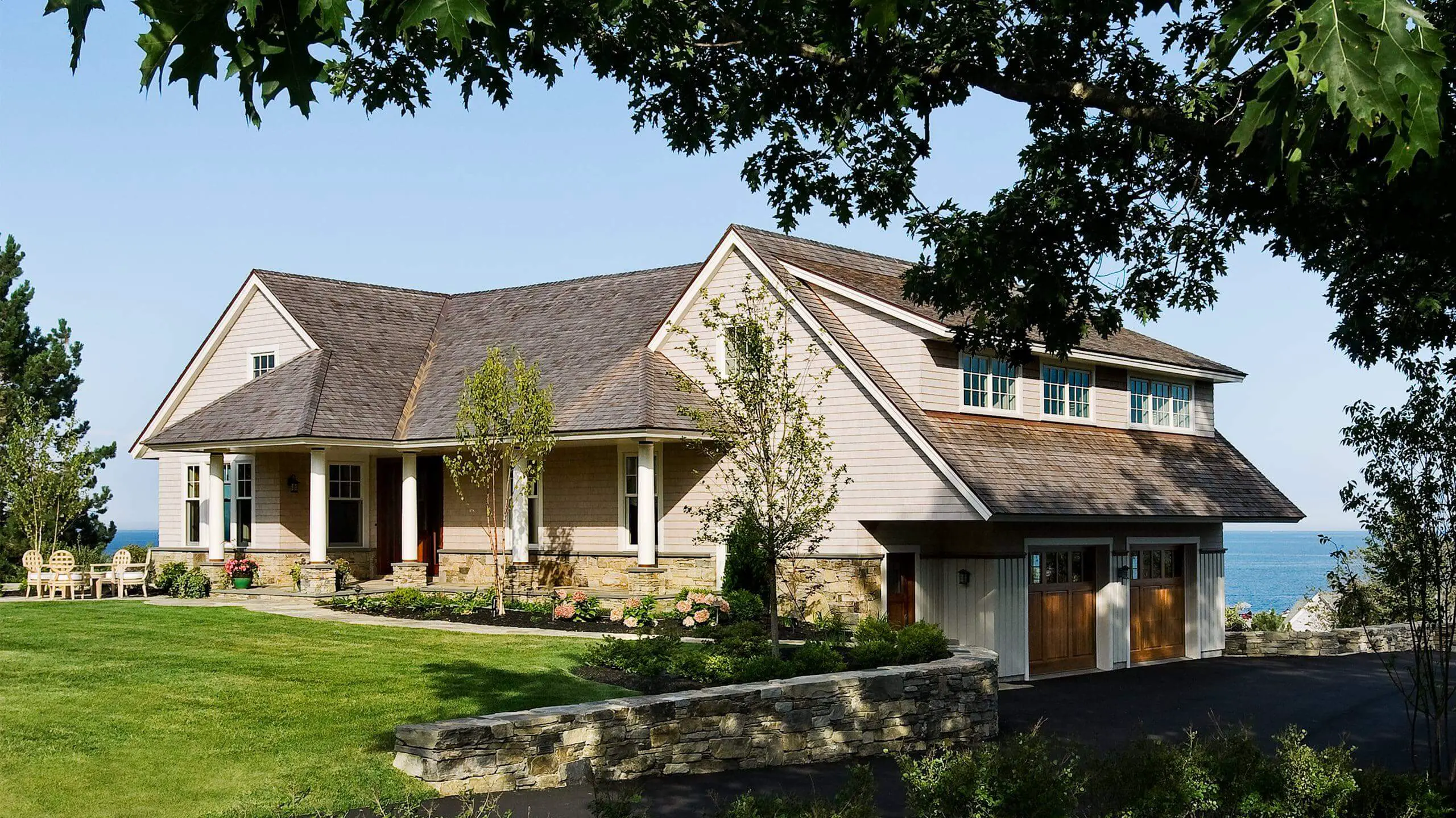Coastal home with stone base, wooden garage, and blue water view