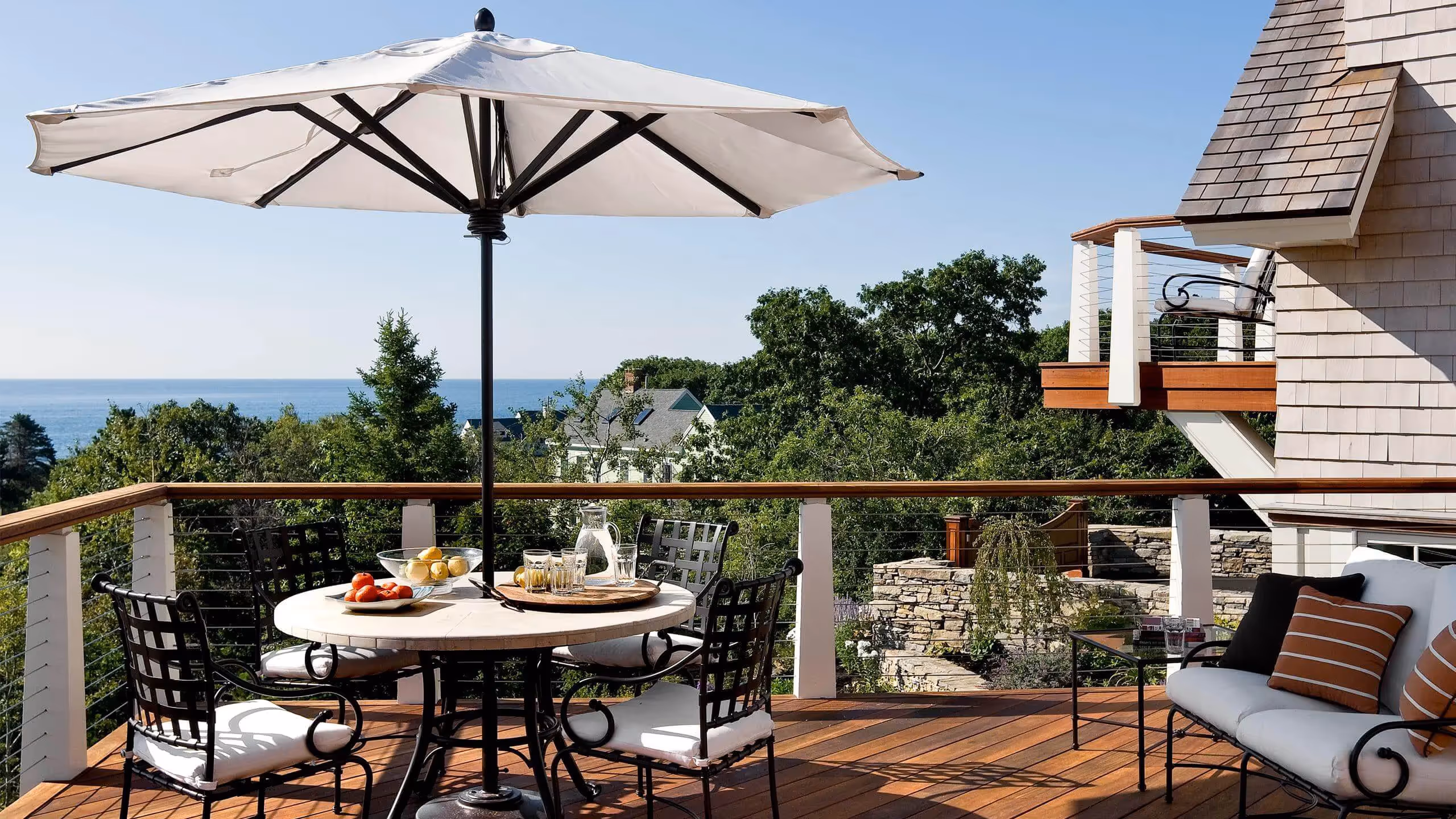 Sunny deck with ocean view, dining table, umbrella, and comfortable seating