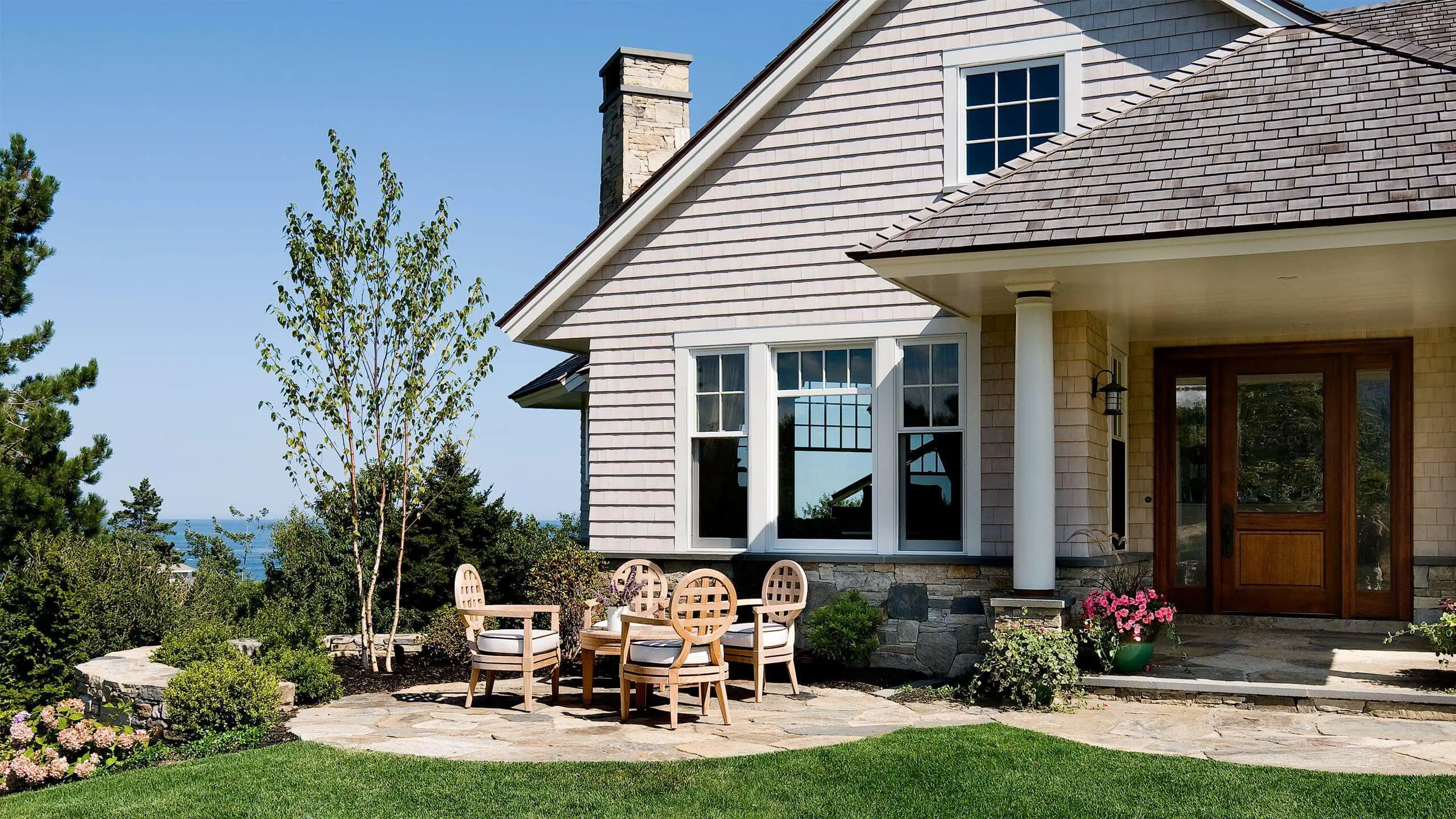 Coastal home with stone patio, wooden chairs, and ocean view