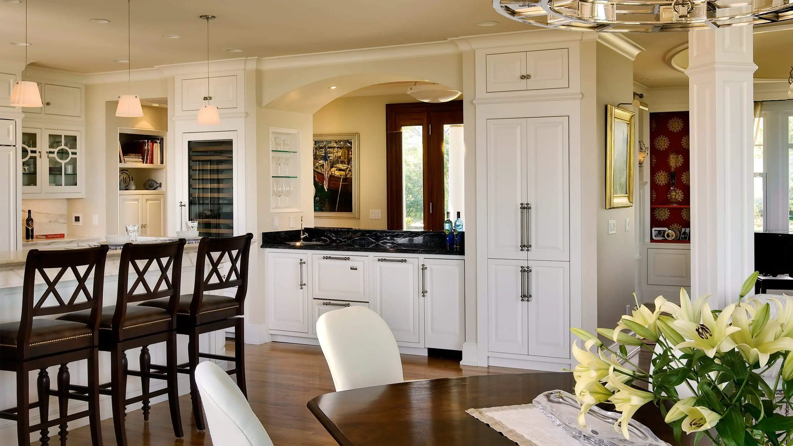 Elegant white kitchen with bar stools, wine fridge, and yellow lilies
