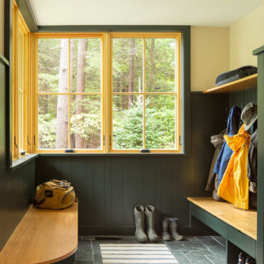 Mudroom with wooden bench, boots, raincoat, and forest view through windows