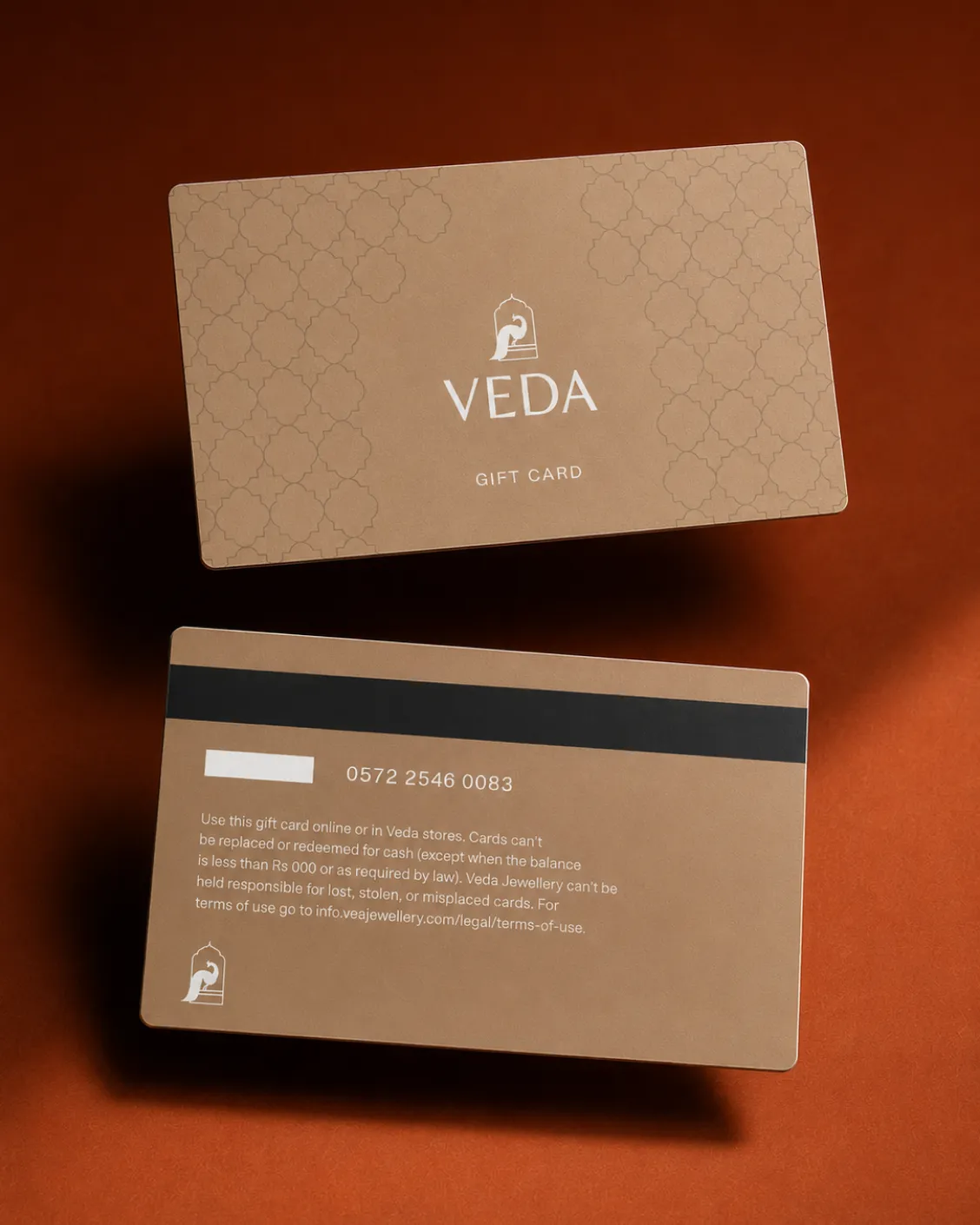 Two brown Veda gift cards on a brown surface, one showing front logo, the other with card number and terms.