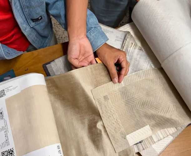 Hands examining fabric samples with different beige and cream textured patterns on a table.
