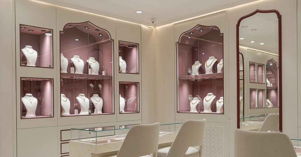 Modern jewelry store interior with display cases showing necklaces on white busts and two chairs at a glass counter.