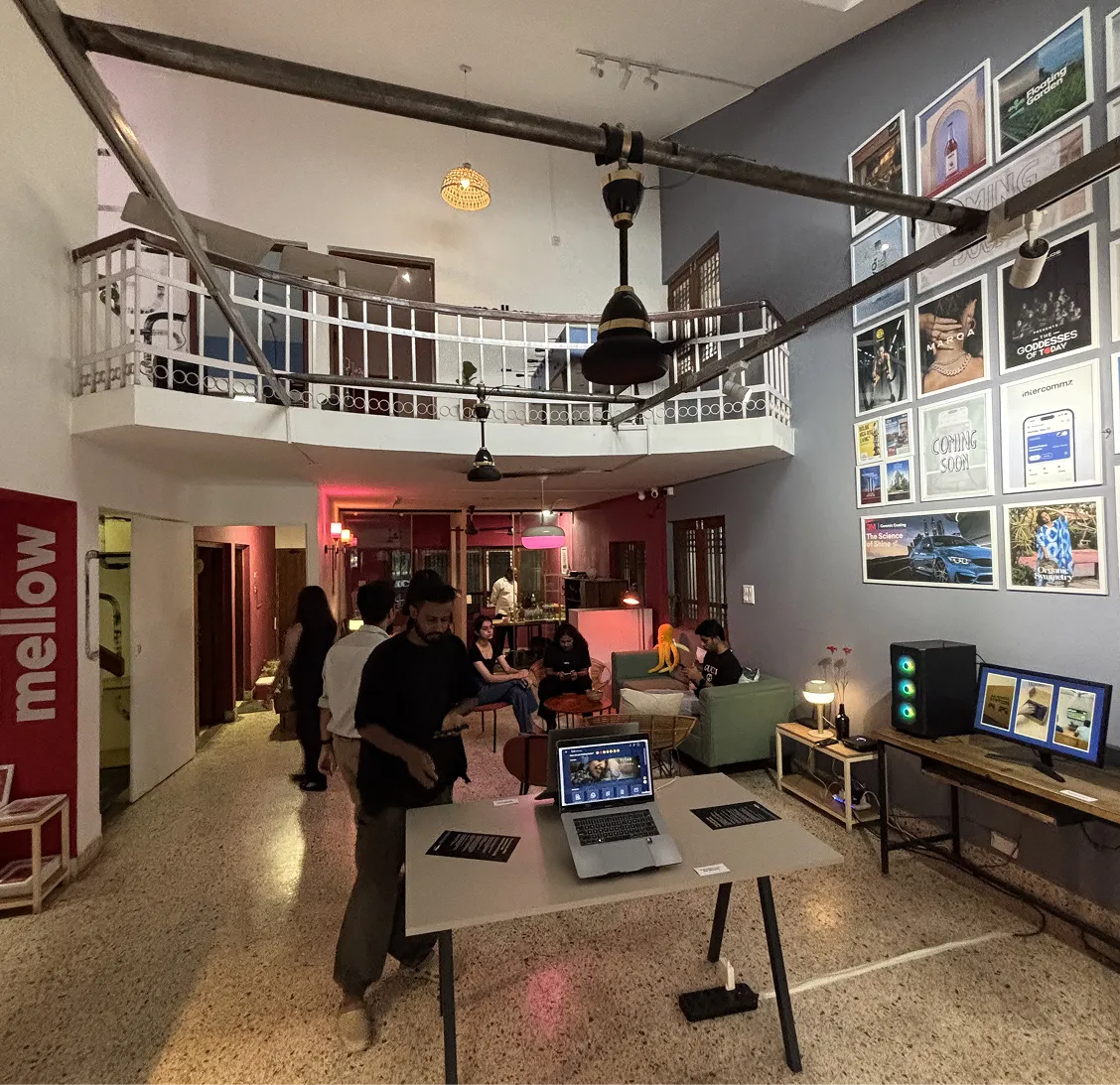 Cozy workspace with people, laptops on a table, artwork on walls, and a balcony inside the room.