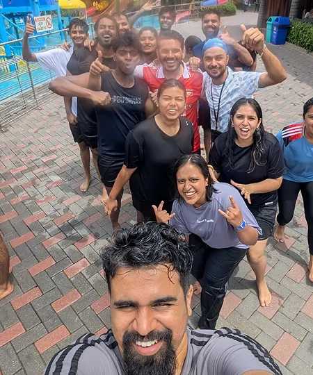 Group of smiling young adults posing for a selfie outdoors on a brick pathway near a colorful playground.