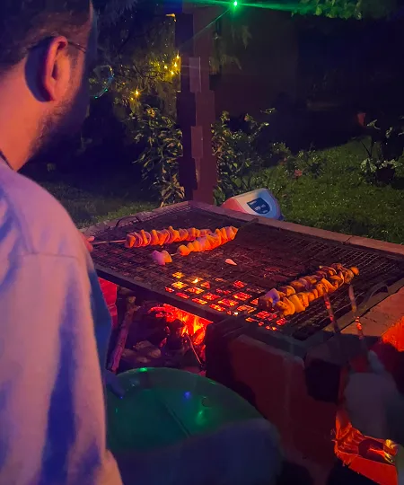 Person grilling skewers with meat over open flame grill outdoors at night.
