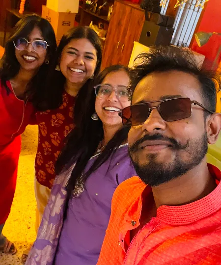 Four smiling friends in colorful traditional clothing taking a close-up group selfie indoors.