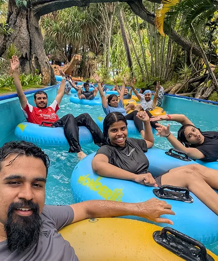 A group of people enjoying a water park ride on blue inner tubes surrounded by trees.