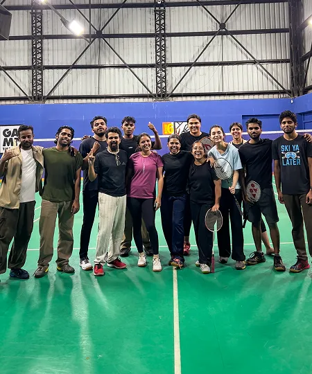 Group of people standing on badminton court holding rackets, smiling and posing for a photo.