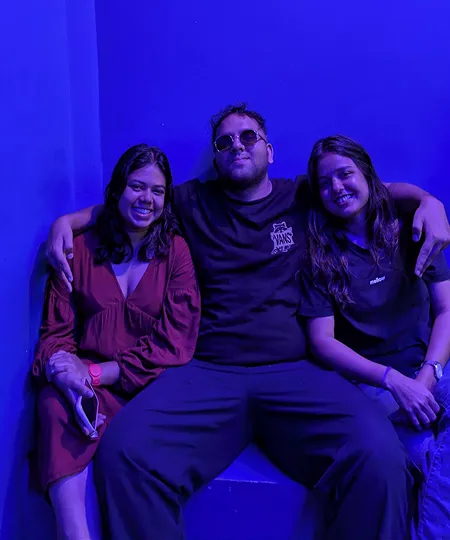 Three friends sitting closely together with arms around each other in blue lighting.