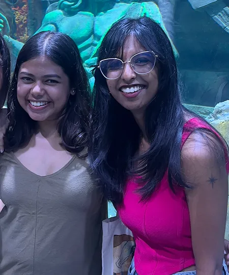 Two smiling women standing side by side in front of an aquarium exhibit with a sculpture in the background.