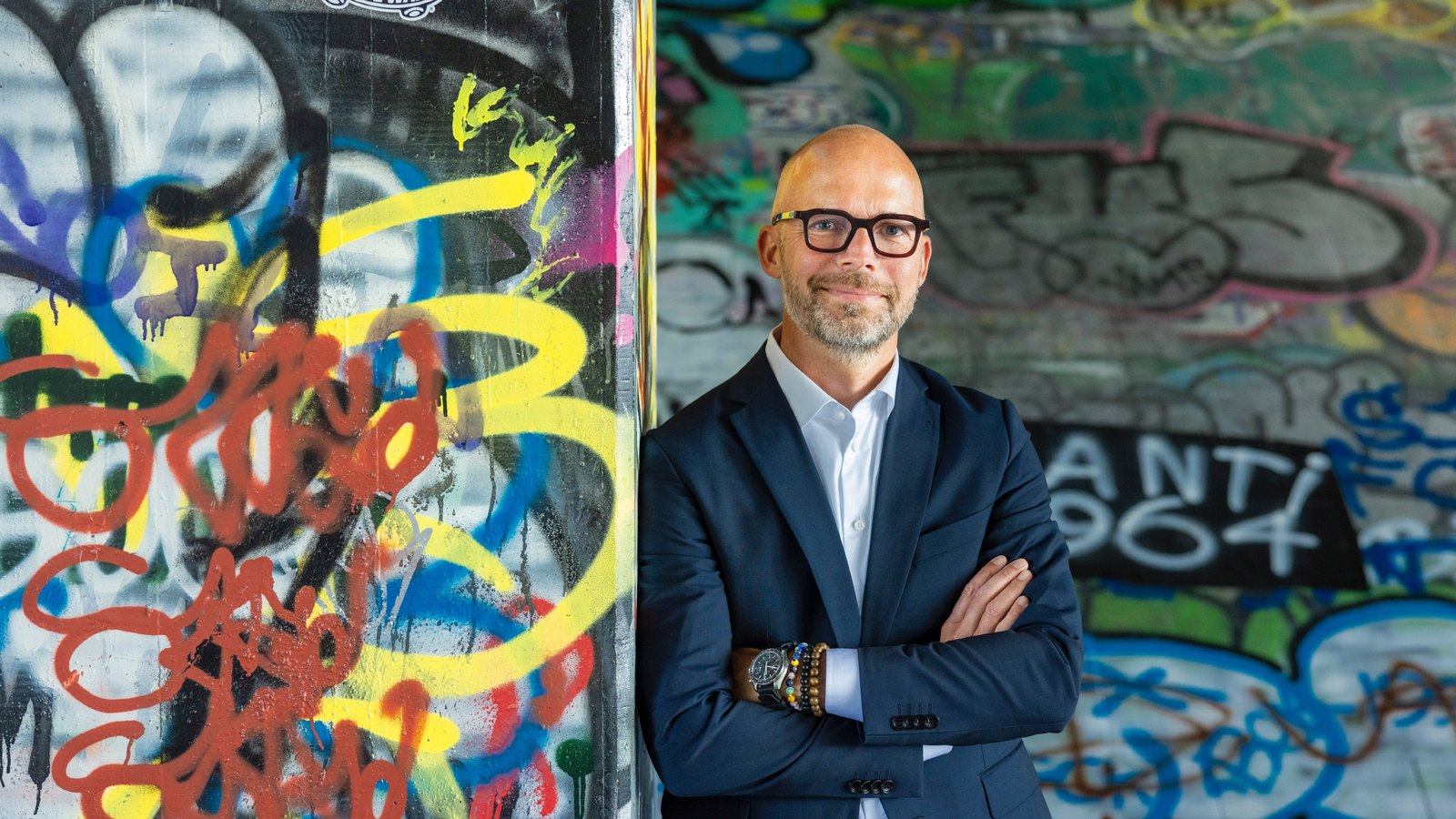 Peter Sorgenfrei with arms folded in front of a graffiti wall
