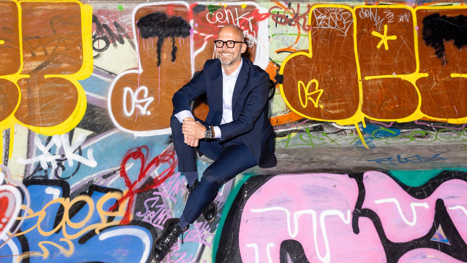 Peter Sorgenfrei seated against a colourful graffiti wall