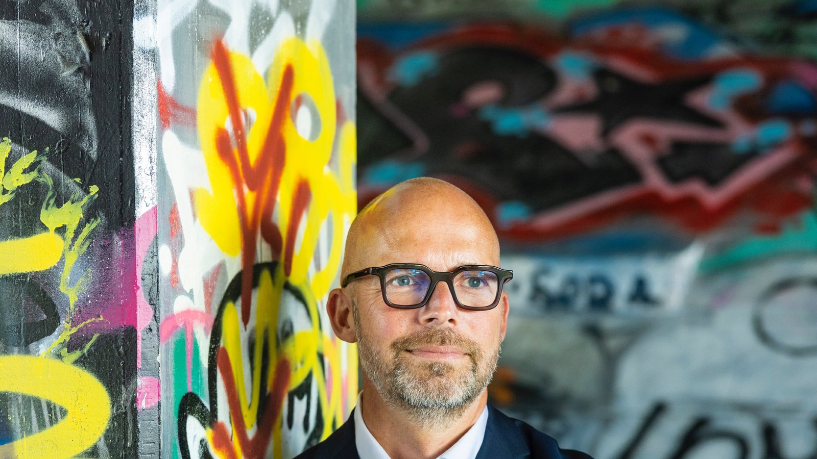 Peter Sorgenfrei looking directly at the camera in front of a graffiti wall