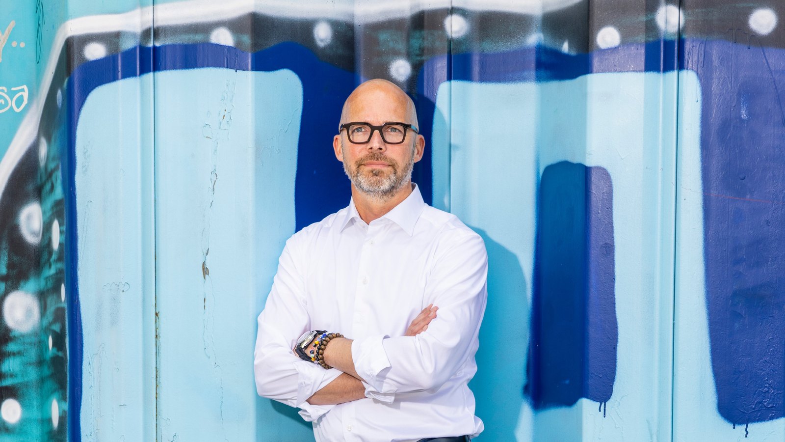 Peter Sorgenfrei with arms crossed against a blue painted wall