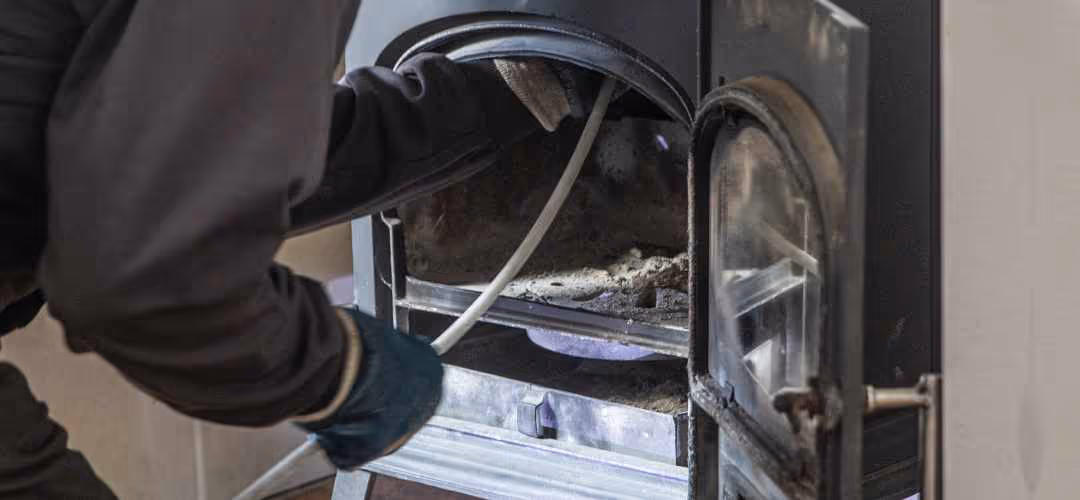 Person cleaning or inspecting the inside of a wood-burning stove with a pipe or hose.