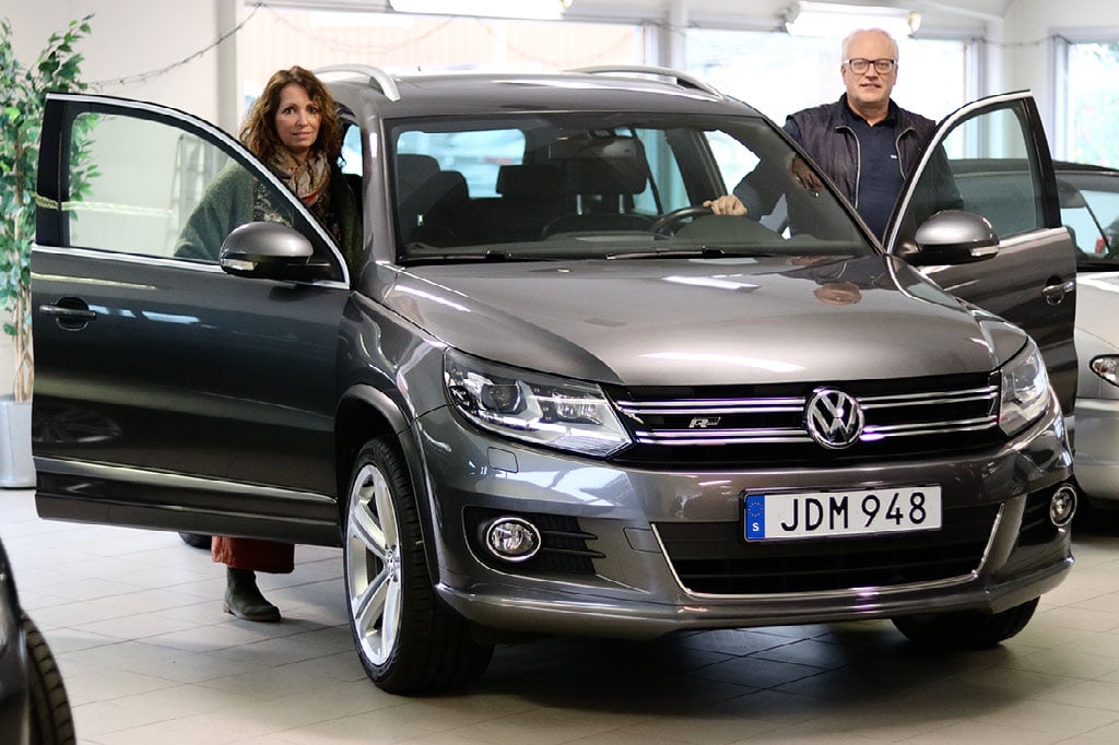 A man and woman standing beside a gray Volkswagen SUV with its front doors open inside a showroom.