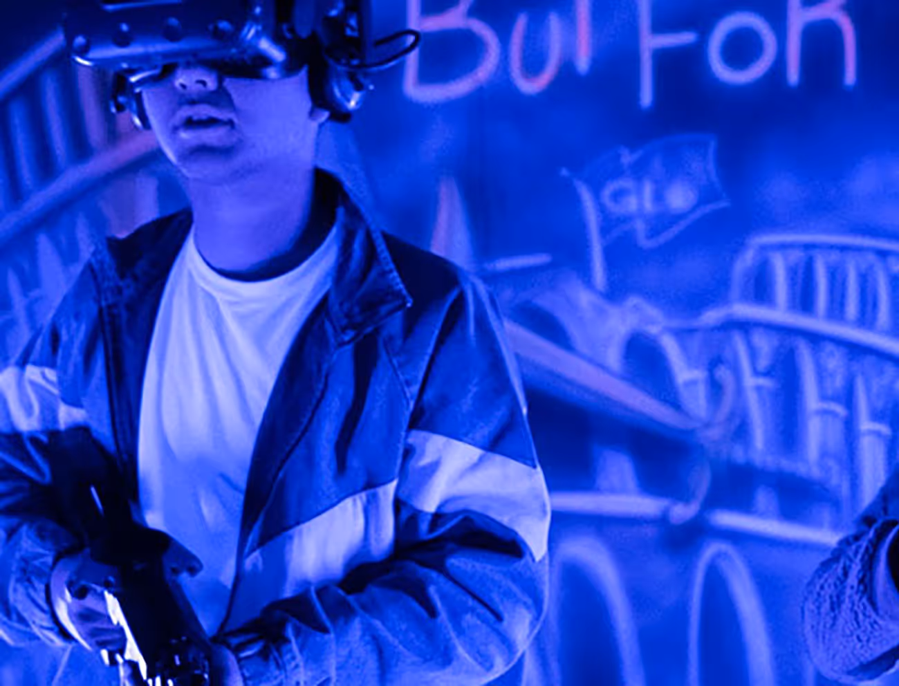 A person wearing a virtual reality headset holds a controller, with a blurred background featuring graffiti art illuminated in blue light.