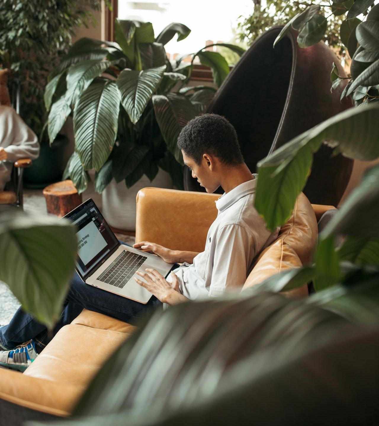 Woman wearing glasses and earphones, working on a laptop at a wooden table with a smartphone and newspaper.