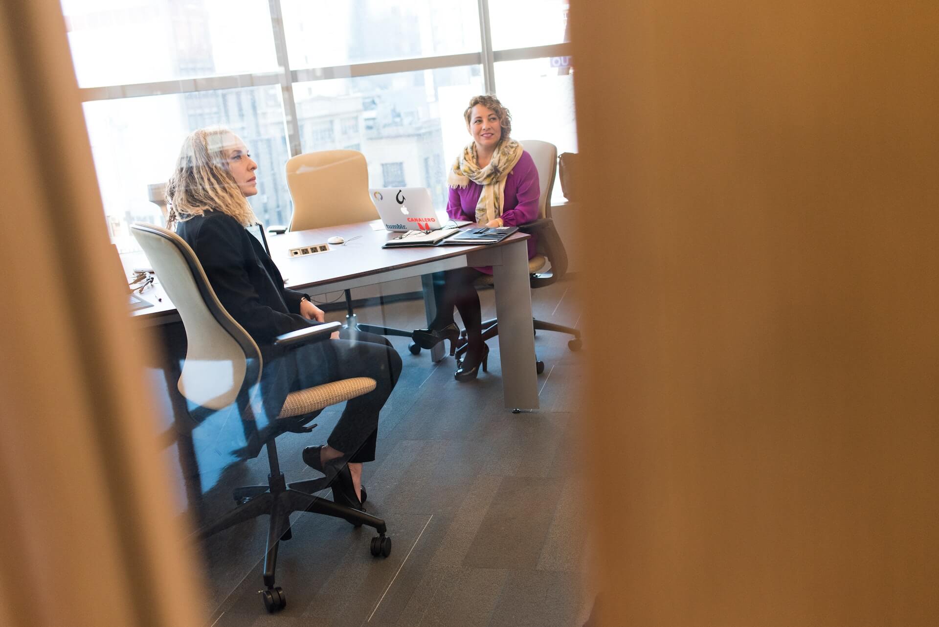 Two colleagues meeting in an office viewed through a doorway