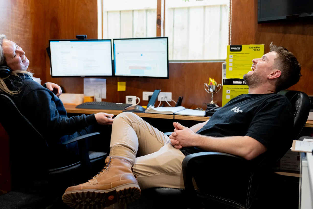 Jordan Statham and Darlene McIntyre laughing in the office, leaning back at their desks