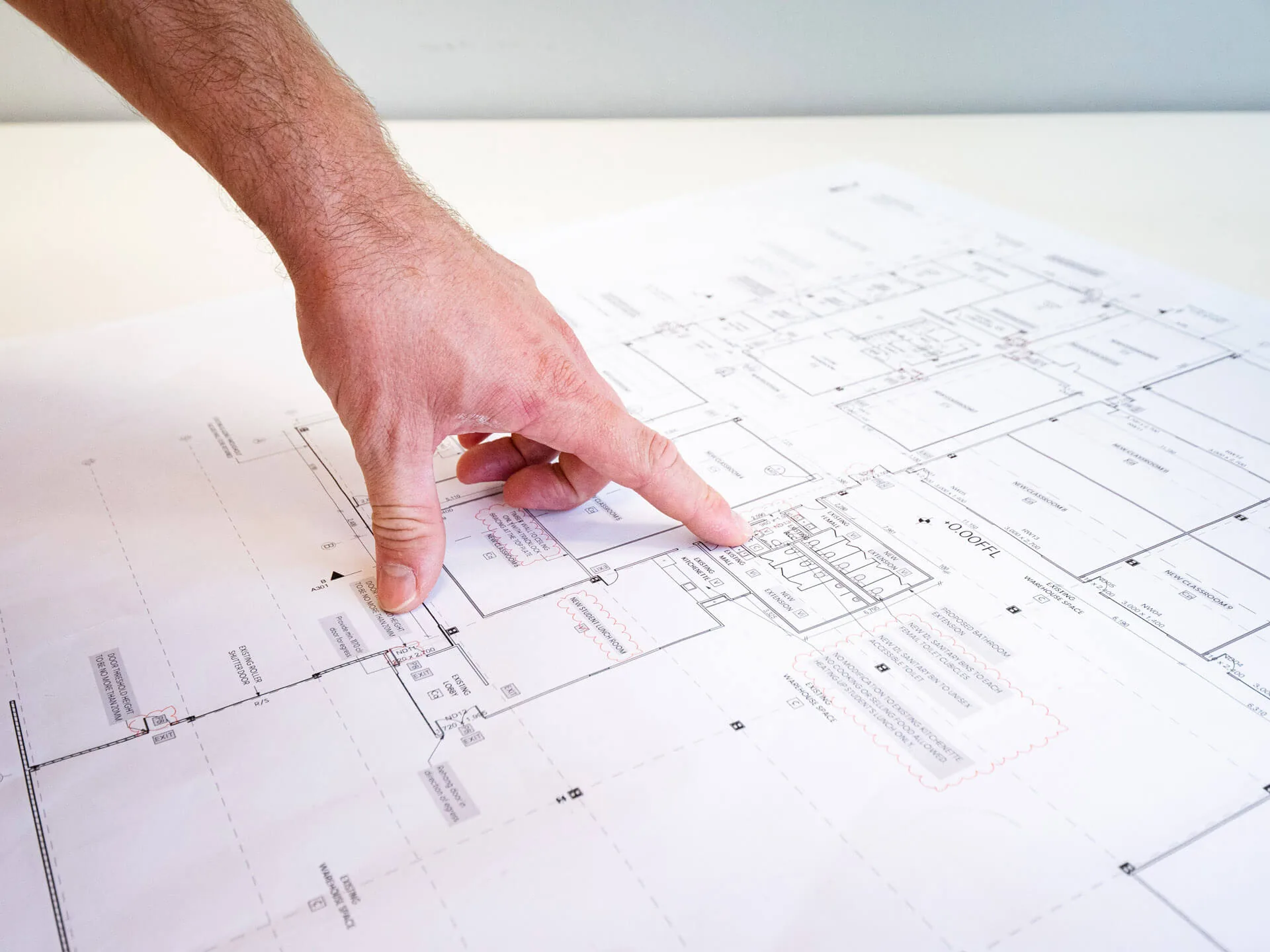 A hand tracing a circuit on a large printed electrical plan
