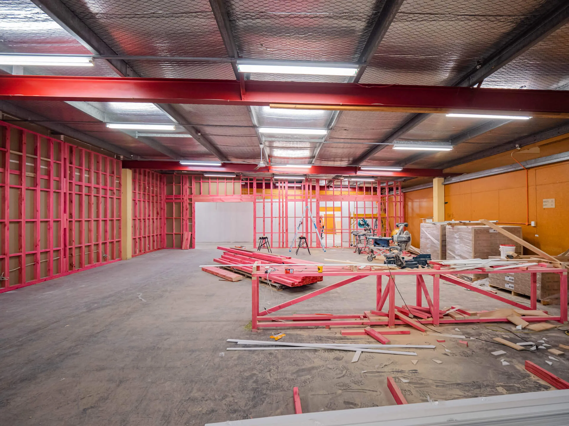 A warehouse interior mid fitout, red steel framing under new strip lighting
