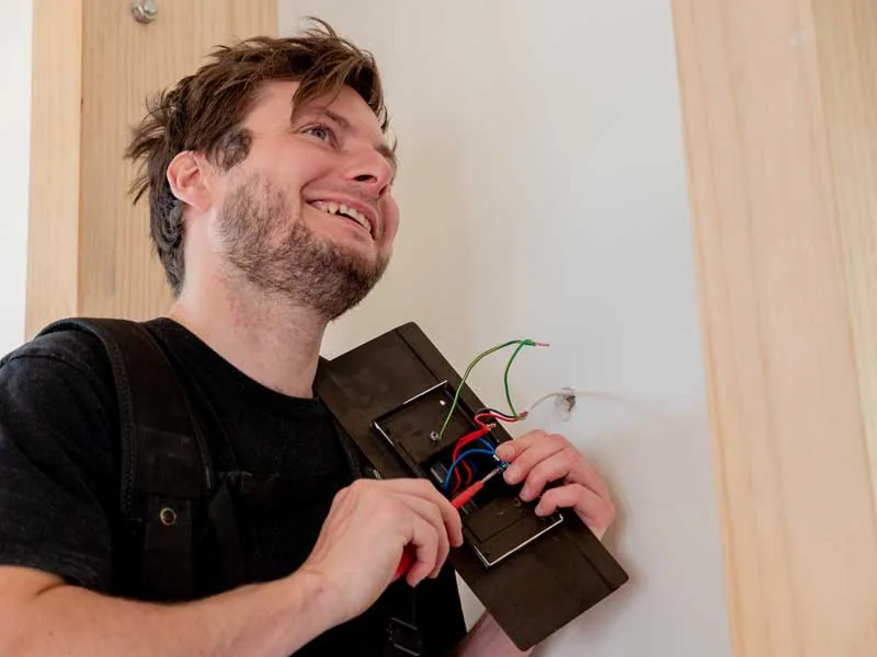 A smiling electrician wiring a switch plate on an interior wall