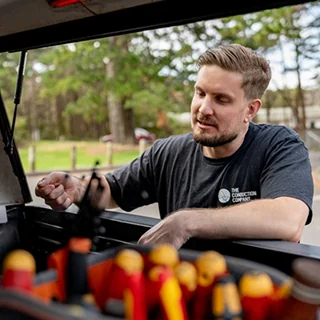 An electrician in a branded shirt reaching into the back of a van packed with hand tools