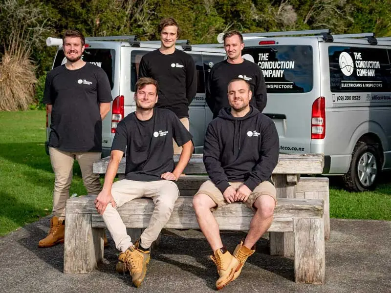 Five Conduction Company electricians in branded shirts in front of two company vans
