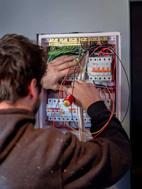 An electrician working inside an open switchboard, hands among red, green and yellow wiring