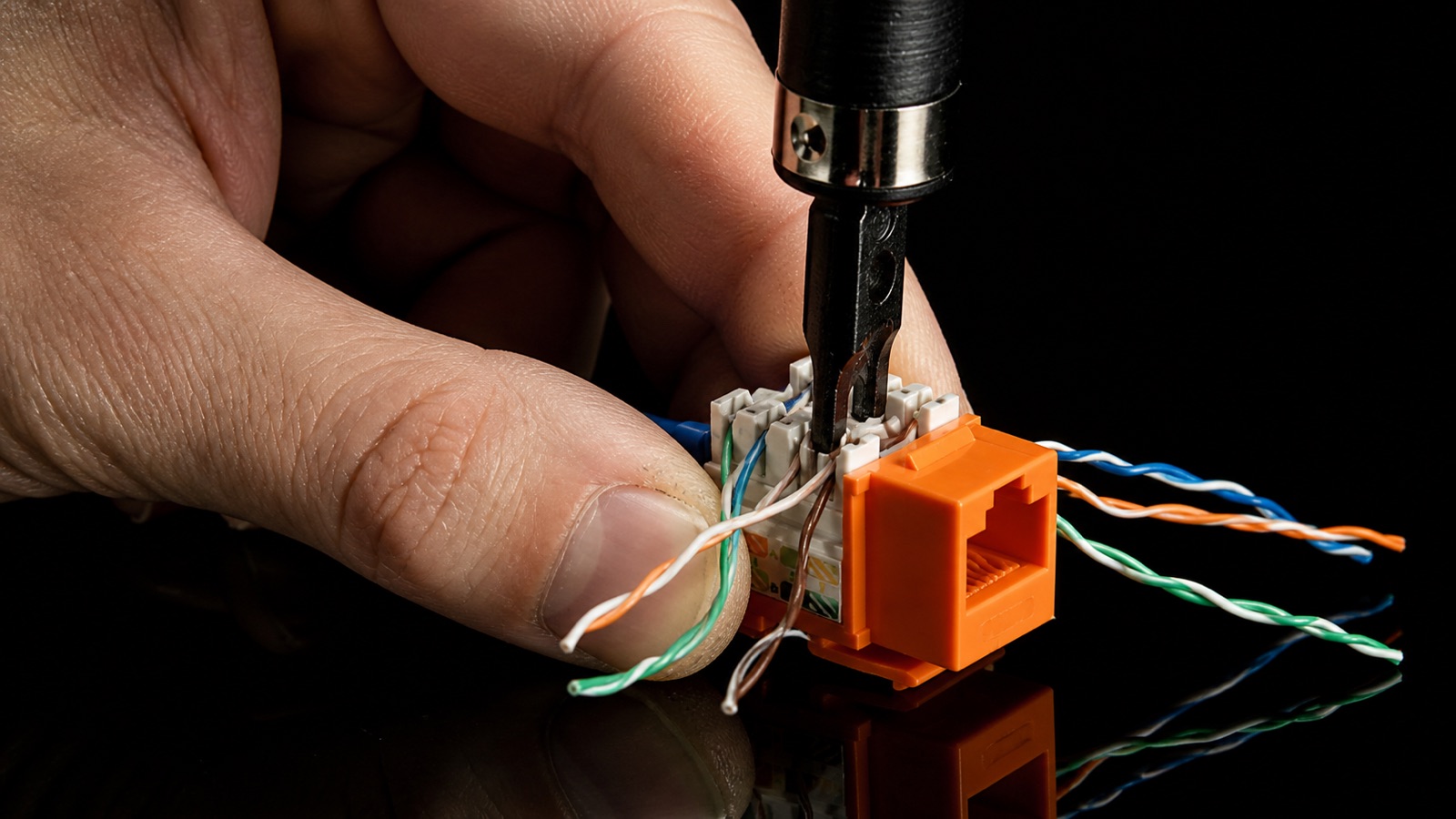 A hand punching down colour-coded network cable pairs into an orange RJ45 keystone jack