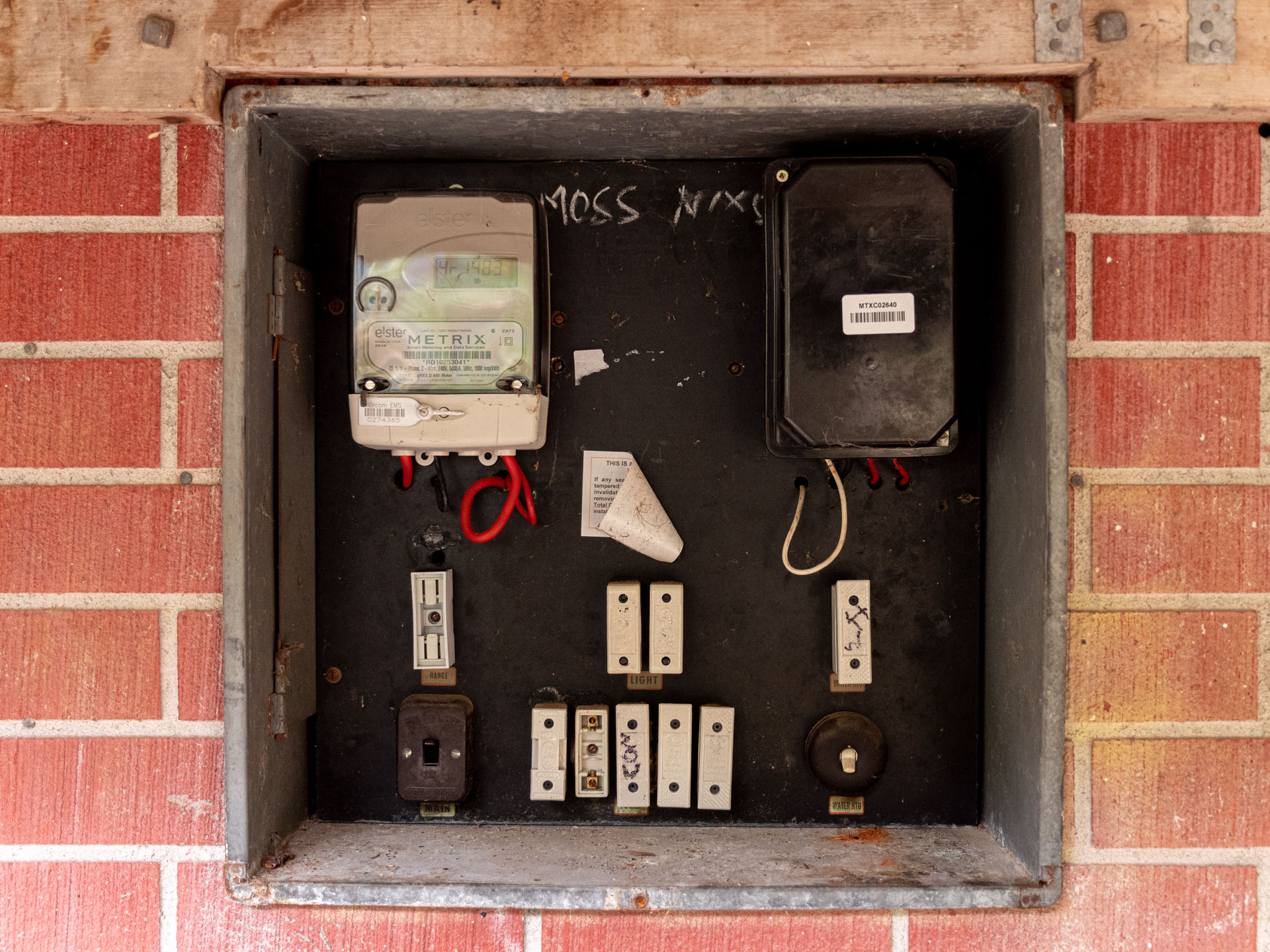An old meter box set into a brick wall, fitted with ceramic rewireable fuses