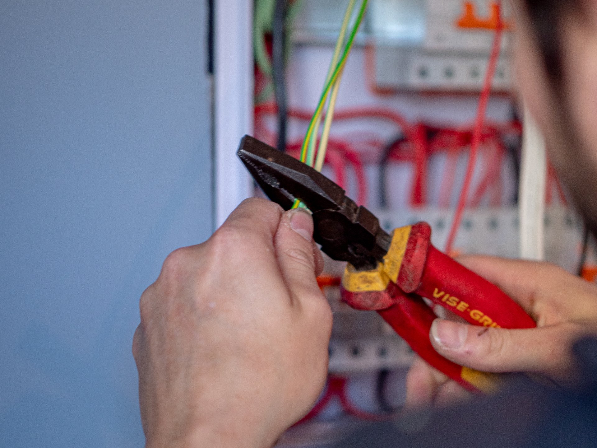 Hands using locking pliers on cable in front of an open switchboard