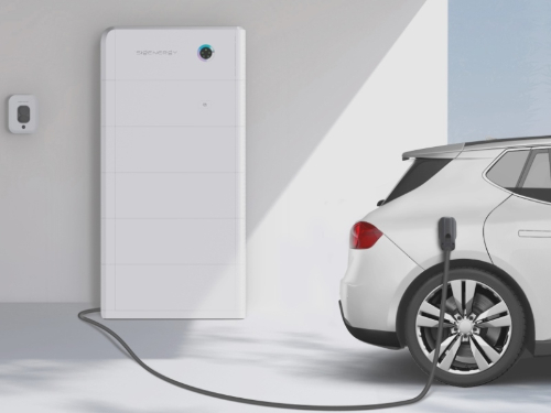 A white home battery unit on a wall beside a car charging on the driveway