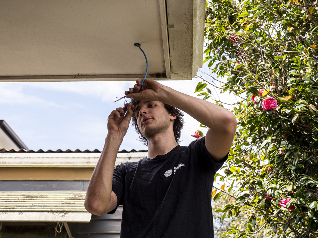 An electrician terminating blue network cable under the soffit of a house