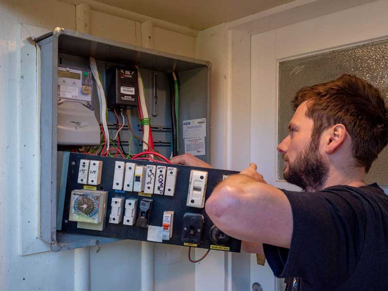 An electrician working inside an open meter box mounted on an exterior wall