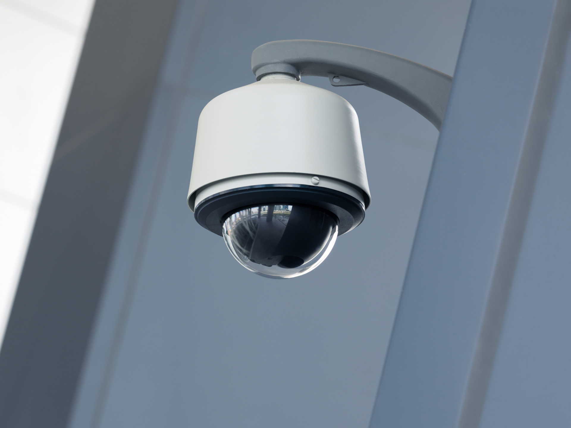 A white PTZ dome security camera mounted on a grey exterior wall
