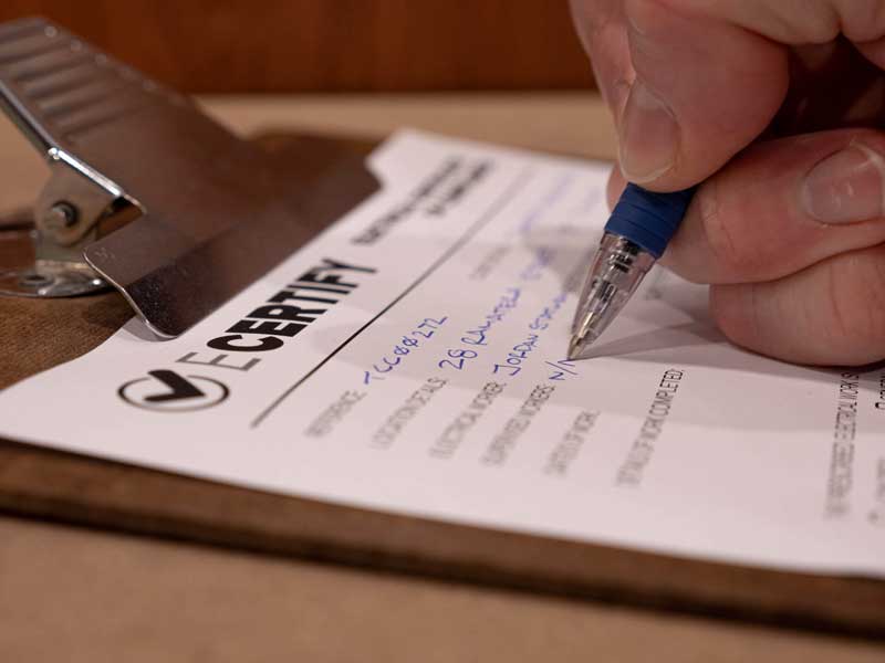 A hand filling in an electrical certificate of compliance on a clipboard