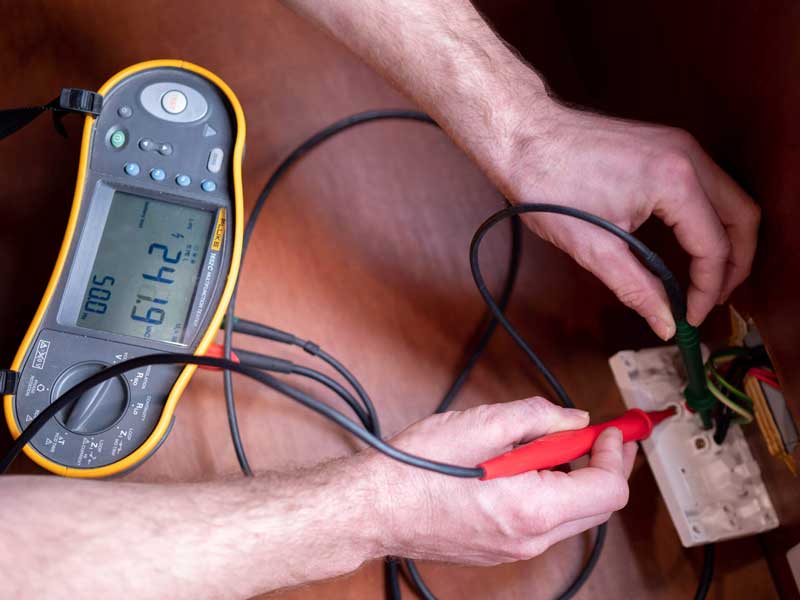 Hands testing a socket outlet with a tester reading 61.42