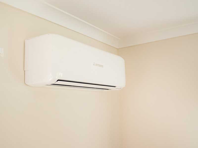 A white wall-mounted heat pump head unit installed high on a lounge wall