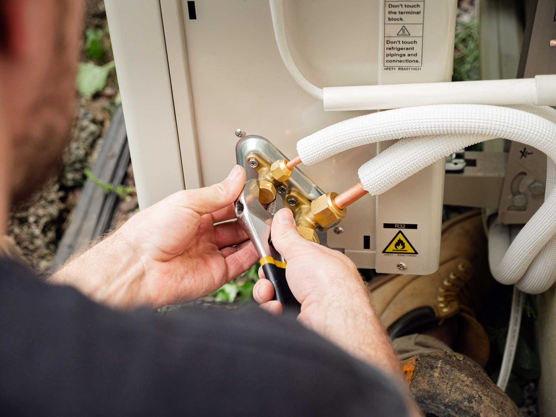 Hands tightening the refrigerant pipe fittings on an outdoor heat pump unit