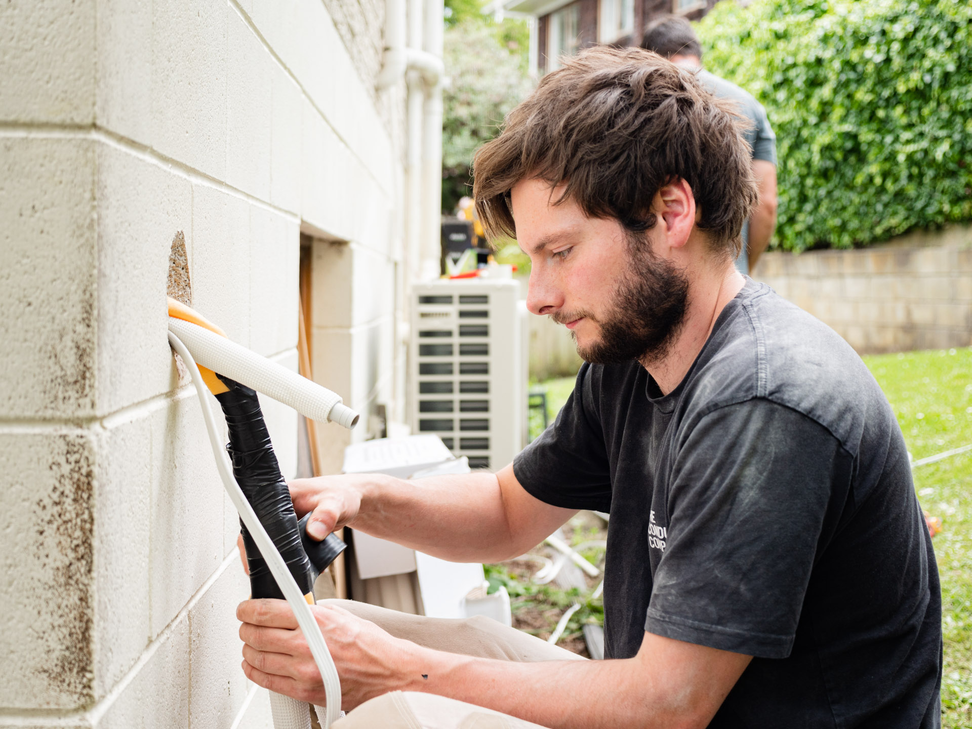 An electrician feeding insulated pipework through a block wall