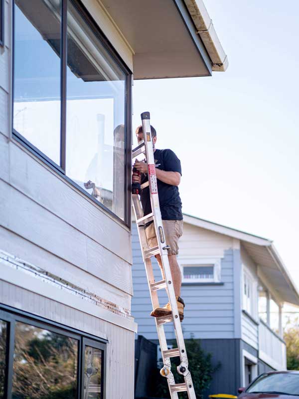 An electrician up a ladder working at the eaves of a two-storey house