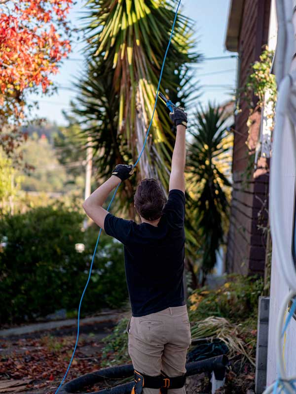An electrician reaching up to pull cable through beside a house