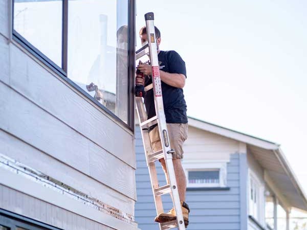 An electrician up a ladder working at the eaves of a two-storey house